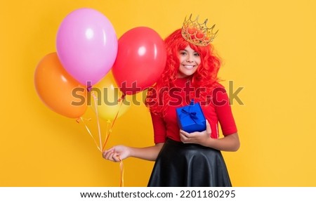 happy child in crown with gift box and party balloon on yellow background