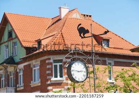 The red tiled rooftop of cottage in sky in russian town. European style. Street clock showing fifteen minutes to three. Sunny summer day. Wind vane decorated with figurines of cat, mouse creatively Royalty-Free Stock Photo #2201187259