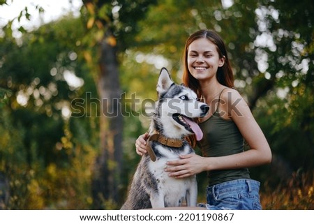 Joyful woman with a husky breed dog smiling while sitting in nature on a walk with a dog on a leash autumn landscape on the background