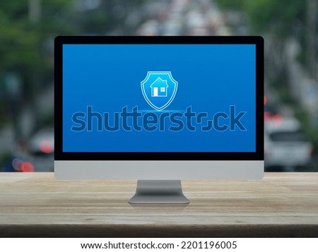 Home with shield flat icon on desktop modern computer monitor screen on wooden table over blur of rush hour with cars and road in city, Business home insurance and security online concept