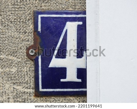 House number (address) four (4) sign, white numbered blue plate (closeup) against gray wall of old building background. Grunge, texture, wallpaper