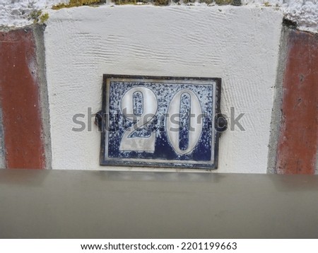 House number (address) twenty (20) sign, white numbered blue plate (closeup) against white wall of old building background. Grunge, texture, wallpaper