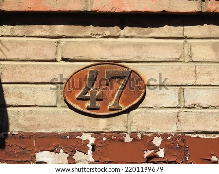 House number (address) forty seven (47) sign, black numbered orange rusty plate (closeup) against brick wall of old building background. Grunge, texture, wallpaper