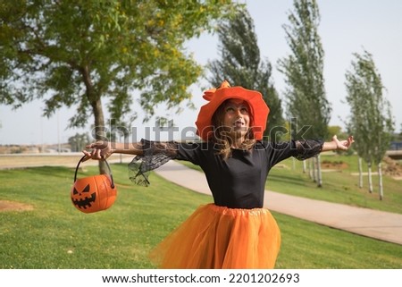 Girl in black shirt, witch hat and orange skirt with pumpkin in hand and open arms celebrating halloween. Autumn concept, trick or treat, party, pumpkin.