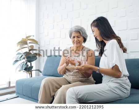 Portrait of Asian senior woman grey short hair holds pill and a glass of drinking water from young adult daughter, taken daily medicine or vitamin supplements, elderly healthcare and medical at home.