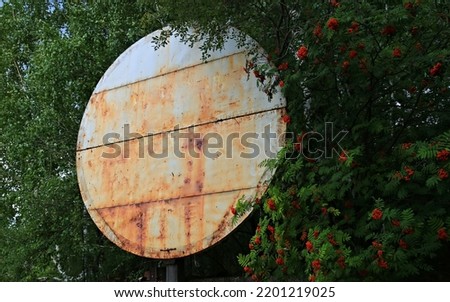 a large rusty sign for advertising against the background of a green mountain ash forest