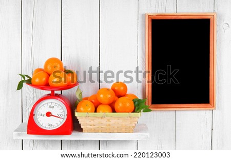 Tangerines on scales and in a basket on a wooden shelf. A framework on a wooden background.