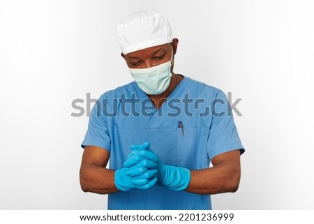 Black surgeon doctor man in blue coat white cap surgeon mask sterilizes blue gloves with aseptic technique, isolated on white background. Adult black african american practicing surgeon portrait Royalty-Free Stock Photo #2201236999