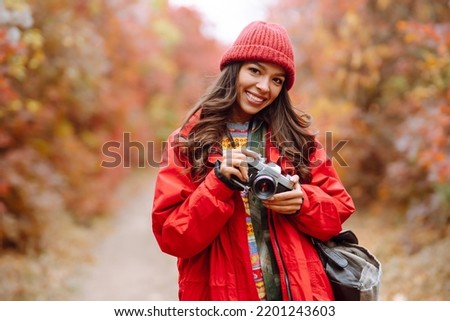 Beautiful woman taking pictures  in the autumn forest. Smiling woman enjoying autumn weather. Rest, relaxation, lifestyle concept.