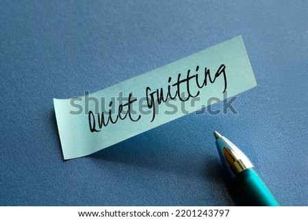 Text words Quiet Quitting on mint green paper note with pen on blue paper. Close-up on sticky note. It means refusal to do more work than necessary at workplace, employee disengagement. Royalty-Free Stock Photo #2201243797
