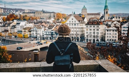 Young beautiful pretty blonde tourist girl in warm hat and coat with backpack walking at cold autumn in Europe city enjoying her travel in Zurich Switzerland Royalty-Free Stock Photo #2201257855