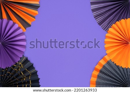Halloween decorations. Orange, black and purple paper fans on a purple. Bright multicolored paper fans of traditional Halloween colors on a purple background with copy space.