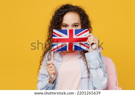 Young smiling happy black teen girl student she wear casual clothes backpack bag hold cover mouth with british flag isolated on plain yellow color background. High school university college concept