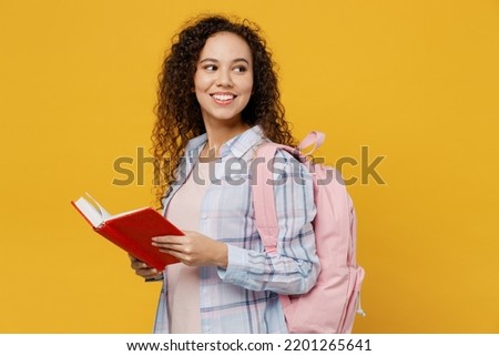 Side view young smiling happy black teen girl student she wear casual clothes backpack bag read book look aside on area isolated on plain yellow color background High school university college concept Royalty-Free Stock Photo #2201265641
