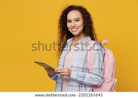 Side view young smiling ahppy fun cool black teen girl student she wear casual clothes backpack bag tablet pc computer isolated on plain yellow color background. High school university college concept Royalty-Free Stock Photo #2201265645