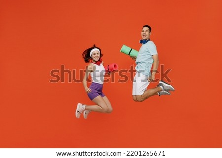Full body young fitness trainer instructor sporty two man woman in headband t-shirt jump high hold yoga mat spend weekend in gym isolated on plain orange background. Workout sport lifestyle concept