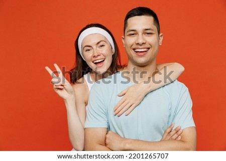 Young smiling happy fun fitness trainer instructor sporty two man woman in headband show v-sign t-shirt spend weekend in home gym isolated on plain orange background. Workout sport lifestyle concept