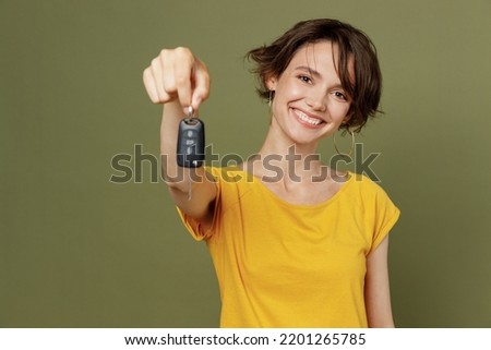 Young satisfied smiling cheerful fun happy woman she 20s wear yellow t-shirt hold in hand give car key fob keyless system isolated on plain olive green khaki background studio People lifestyle concept