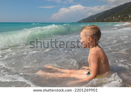 Excited little boy having fun at beach playing with waves. Caucasian kid enjoying summer holidays
