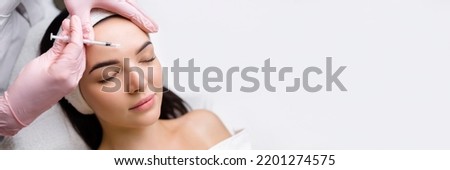 Close up of hands of young cosmetologist injecting botox in female face. She is standing and smiling. The woman is closed her eyes with relaxation Royalty-Free Stock Photo #2201274575
