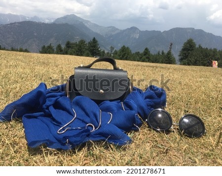 This is a aesthetic picture of bag and sun glasses in greenery at shogran valley Of Pakistan.In this picture you can see the hill view .Beautiful greenery scenes And beautiful sky and mountains 