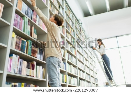 low angle view of students choosing books from variety on racks in library