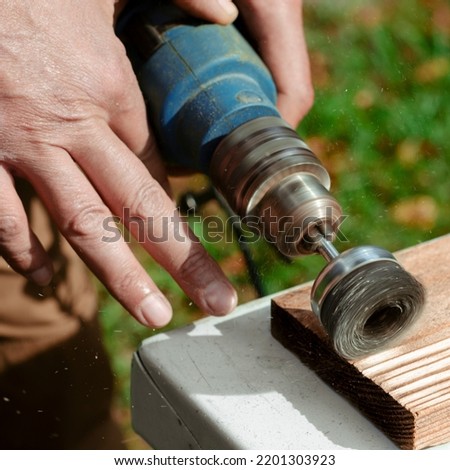 Male hand is holding brushing machine electrical rotating with metal disk sanding a piece of wood.