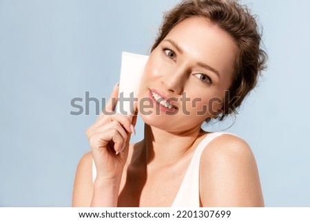 Smiling woman with glowing perfect facial skin holding mock up cosmetics tube of moisturizing cream or foundation for make up. Female advertising skincare products, holds template cosmetic package. Royalty-Free Stock Photo #2201307699