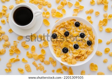 top view of bowl with corn flakes and milk near cup of black coffee isolated on white