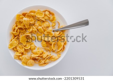 top view of crispy corn flakes in bowl with spoon and milk isolated on white Royalty-Free Stock Photo #2201309531