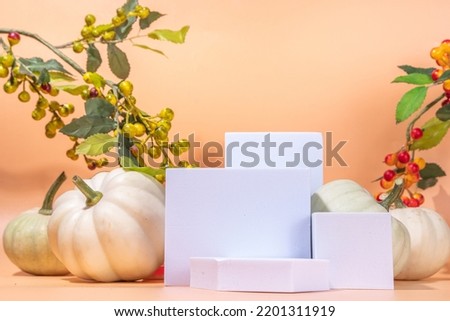 Podium or pedestal with pumpkins for products display or advertising for autumn holidays. Trendy  pedestal and stand mock up composition with decorative berry and pumpkins on beige background