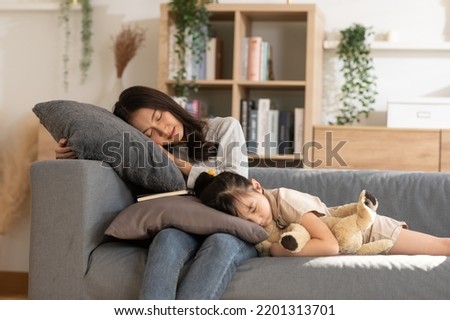 Asian mom sleep with her daughter on couch resting together. Little girl sleep and hug teddy bear on mother legs relax in living room. Tired family sleep at sofa after kid playing at home Royalty-Free Stock Photo #2201313701