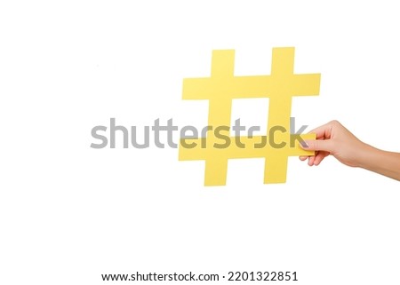 Close up of woman hand holding large yellow paper hashtag symbol, hash sign of famous media content, social media marketing and blog promotion, posing over white studio background wall with copy space