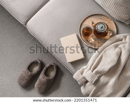 Cashmere sweater, reading and serving tray on gray sofa. Warm weekend at home aesthetics. Detail of cozy scandinavian winter interior. Warm soft winter slipper on carpet at home Royalty-Free Stock Photo #2201351471