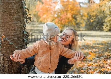 Happy mother and daughter are walking in the autumn park. Beautiful family in warm clothes.