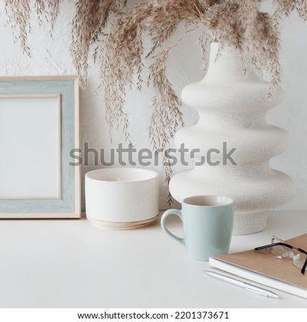 Modern home office workspace with photo frame mockup.  Aesthetic scandy hygge style.Cup coffee, photo frame,planner, vase with grass,aroma candle .Copy space.Neutral colors home design.