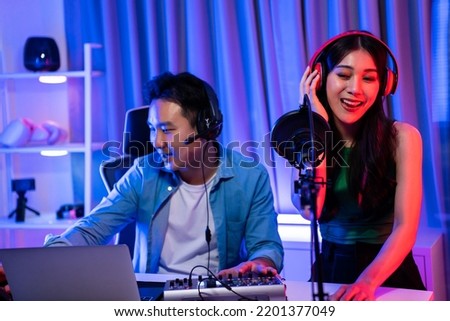 Asian audio DJ man and woman speaks into microphone to broadcasting. Young beautiful female and male blogger influencer wearing headphones and recording morning news podcast show for radio at studio.