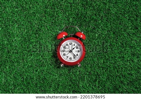 red alarm clock on green turf grass background. half past one o'clock. copy space, game time management concept. opening or closing hours. Ecological sustainable business banner
