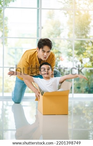 Happy asian family, father having fun with son while pushing carton box in living room.Young family enjoy moving to new home on relocation day. Royalty-Free Stock Photo #2201398749