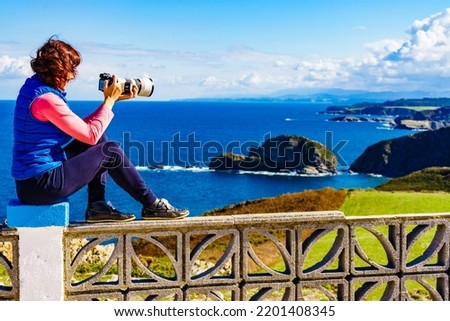 Woman with camera take travel photo from seascape of Atlantic ocean and Asturias coast at Cape Penas in north Spain.