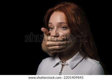A man's hand covers the girl's mouth on a black background. The concept of domestic violence and sexism. Royalty-Free Stock Photo #2201409845