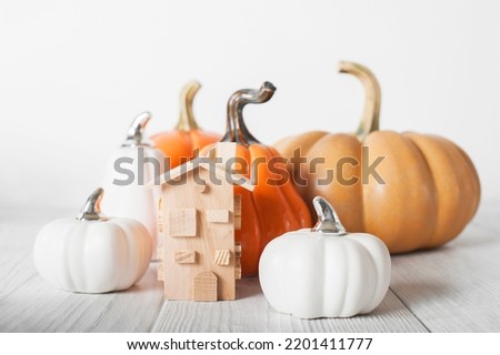 Autumn house insurance, sale, rent concept. White decorative pumpkins and autumn yellow leaves with miniature wooden house close-up and copy space..