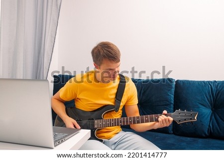 Guitarist is watching a virtual video tutorial at home. hobby. Man learn to play guitar online.  The guy is sitting at home on the sofa and watching an online lesson, learning to play the guitar.