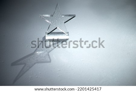 A star made of glass on a silver background in small drops of water. Transparent star. The prize is in the form of a five-pointed star on a metal background.