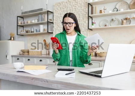 Confused and nervous young beautiful woman in glasses sitting at home calculating her family budget