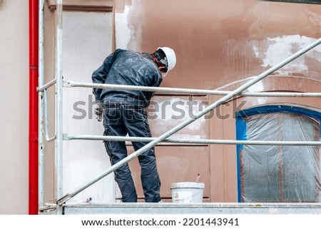 Renovation, restoration, refurbishment. Unrecognizable worker renovating wall of classical style building, standing on scaffolding. Construction worker prepares house facade wall for painting outdoors Royalty-Free Stock Photo #2201443941