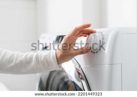 cropped shot of woman hand turn on automatic washing machine or select program with knob on control panel in white bathroom, modern appliances at home Royalty-Free Stock Photo #2201449323