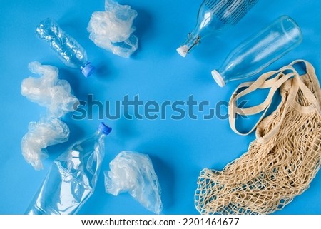 Plastic bottles and several plastic bags opposite one eco-friendly shopping bag and glass bottles on a blue background. The concept of replacing plastic with environmentally friendly materials.  