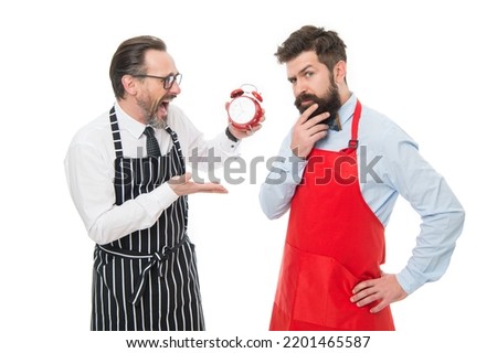 It is lunch time. Men cooks with alarm clock. Man bearded hipster and mature chef apron white background. Start cooking right now. Working hours and lunch break. Lack of time. Check what time is it