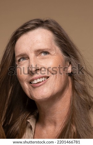 Close up portrait of a Caucasian transgender woman in her 50's on a neutral background, looking up.
